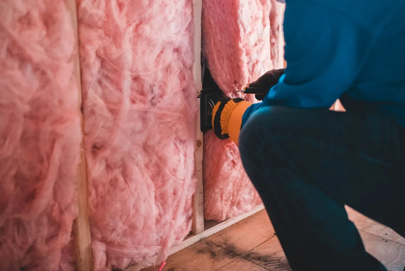 Worker fitting mineral wool insulation between studs